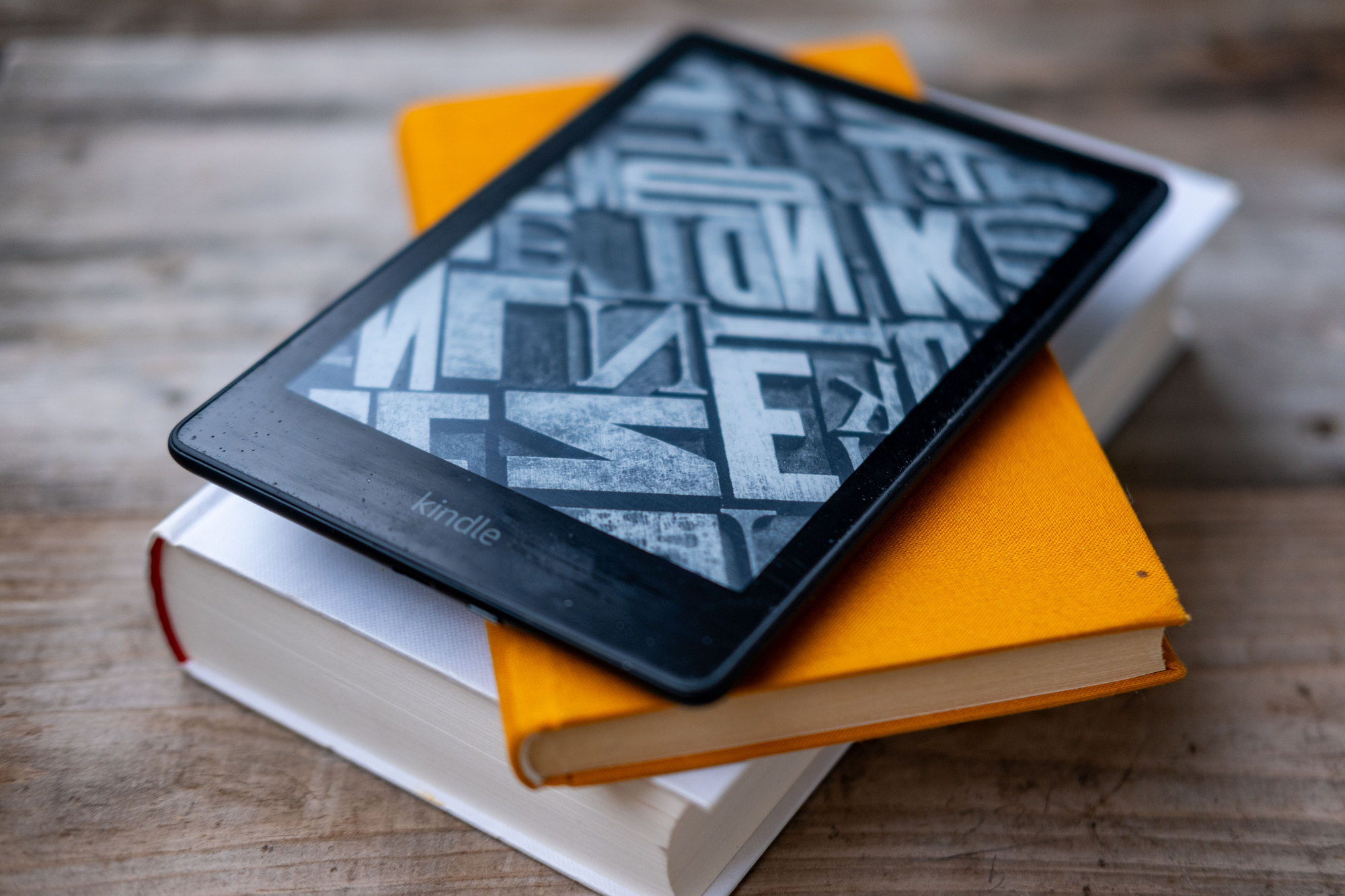 En svart Kindle lesebrett ligger oppå to bøker på et trebord.