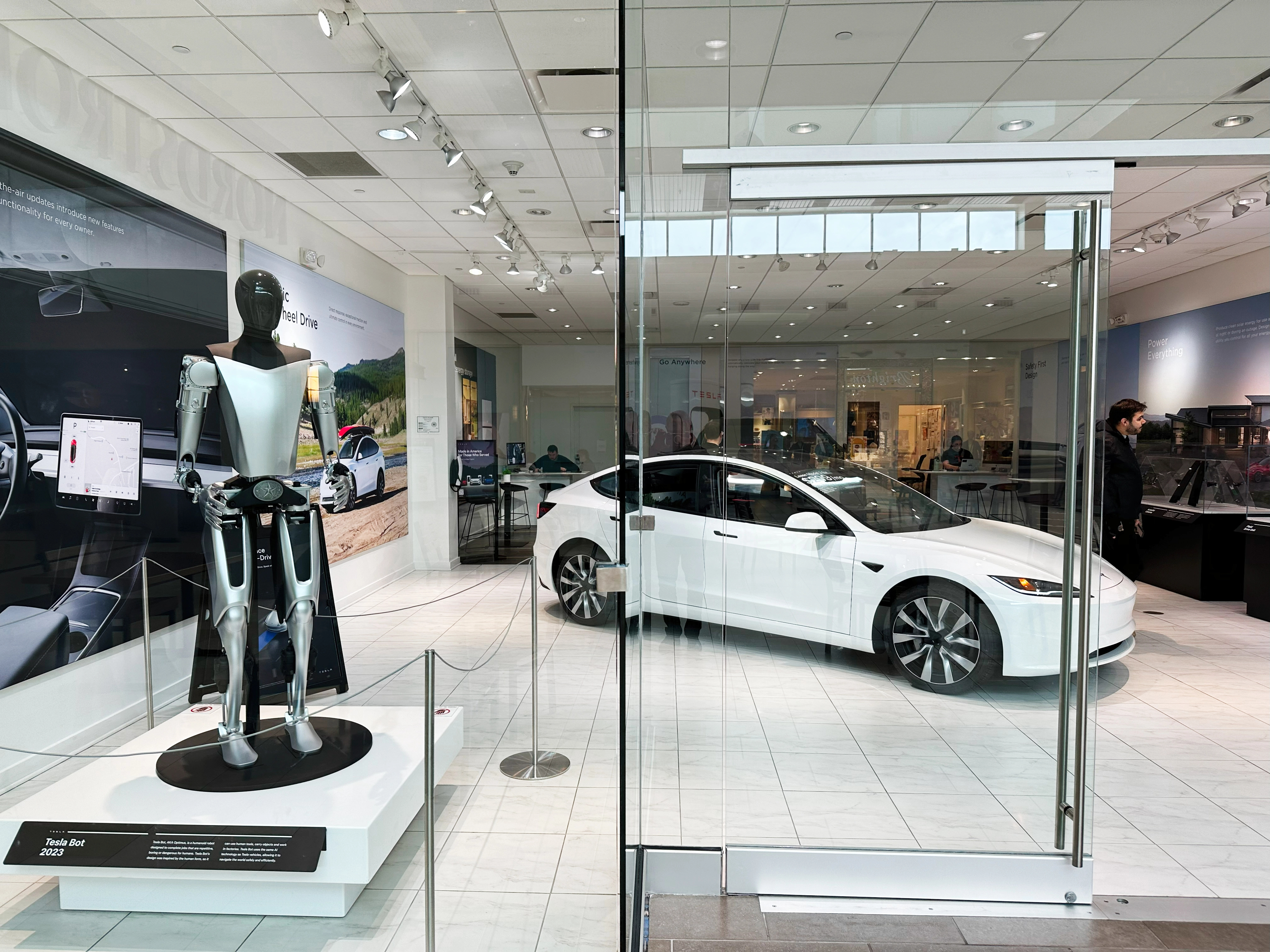 Modern car showroom in the USA features a white Tesla Model S and a metallic Tesla Bot Optimus robot